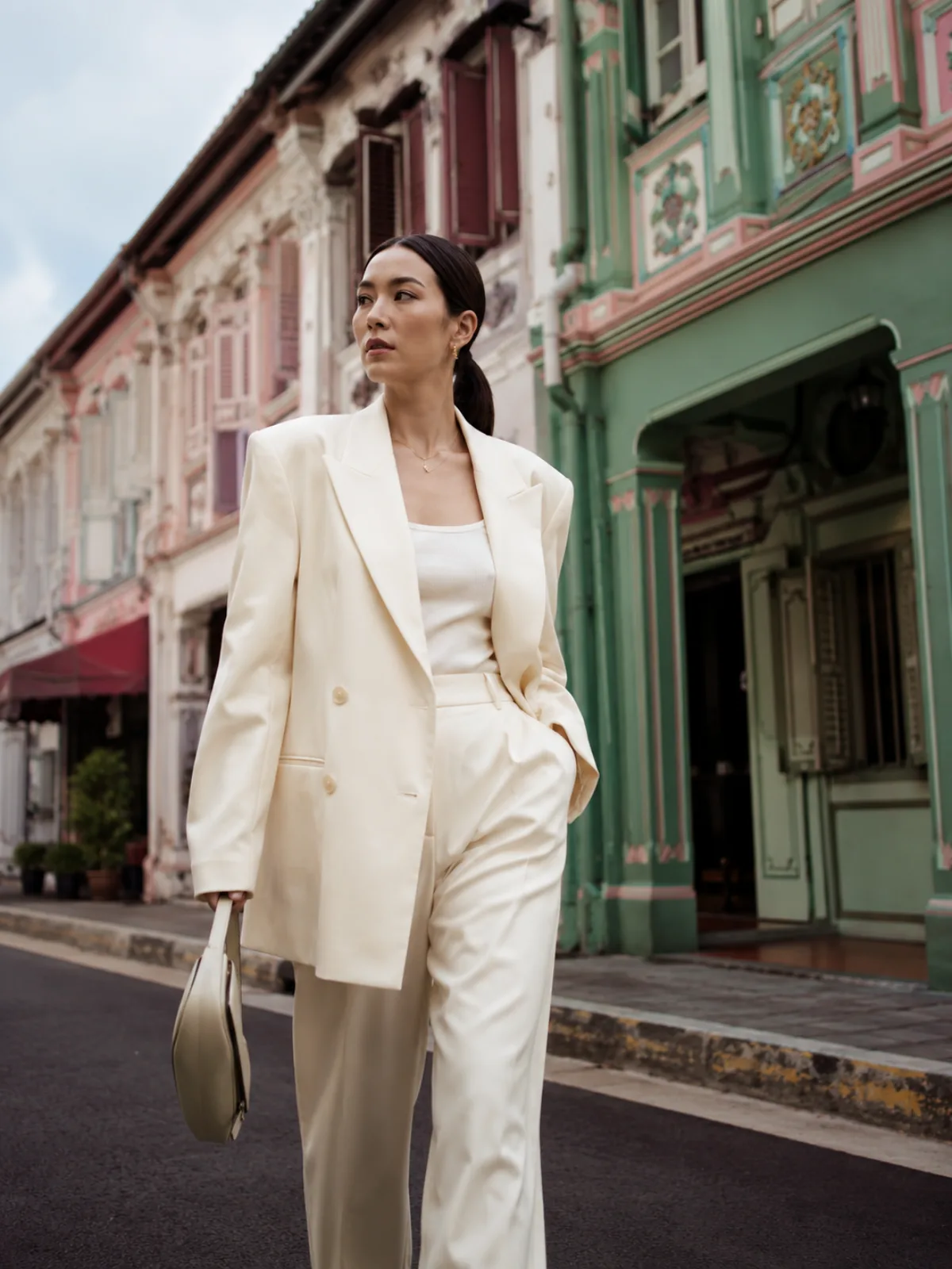 AI model in an ivory tailored blazer walking past Peranakan shophouses
